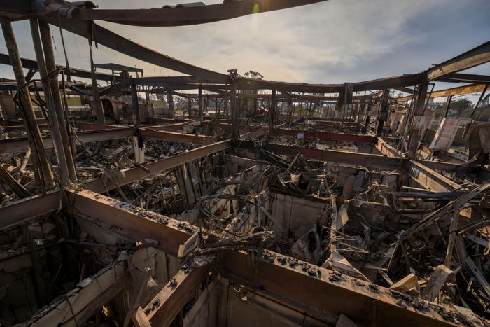 A fire-damaged building with exposed beams and debris beneath a smoky, hazy sky