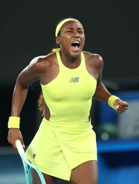 A tennis player erupts in a triumphant yell, wearing a sleeveless sports outfit and headband while clutching a racket in celebration of their victory.