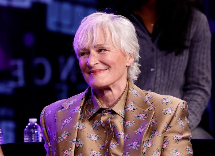 Glenn Close smiles warmly while wearing a floral-patterned blazer, seated on stage at a panel discussion or event.