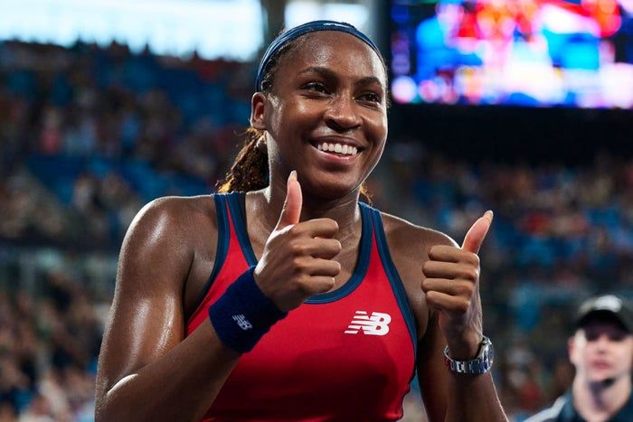 Coco beams with joy, sporting athletic gear and giving a thumbs up after a match, surrounded by a crowd of supporters.