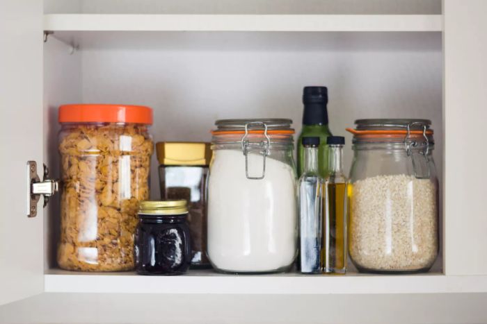 A well-stocked pantry featuring jars and containers of cereals, jam, coffee, sugar, flour, oil, vinegar, and rice