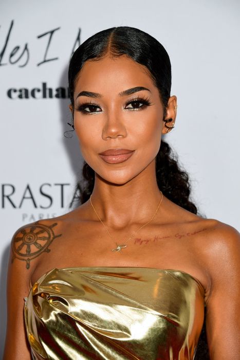 A person is captured at an event, wearing a strapless metallic dress, with elaborate makeup and visible tattoos, striking a pose for the camera.