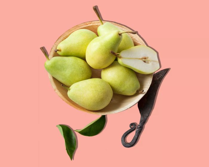 A collection of pears arranged in a bowl against a pink backdrop