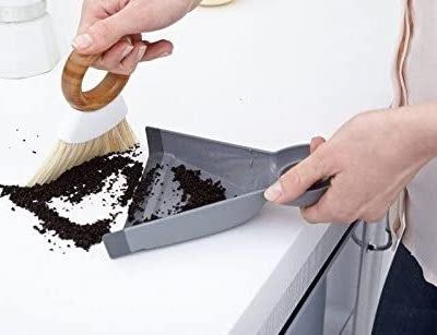 A model is using a mini broom and dustpan to sweep dirt off a counter.