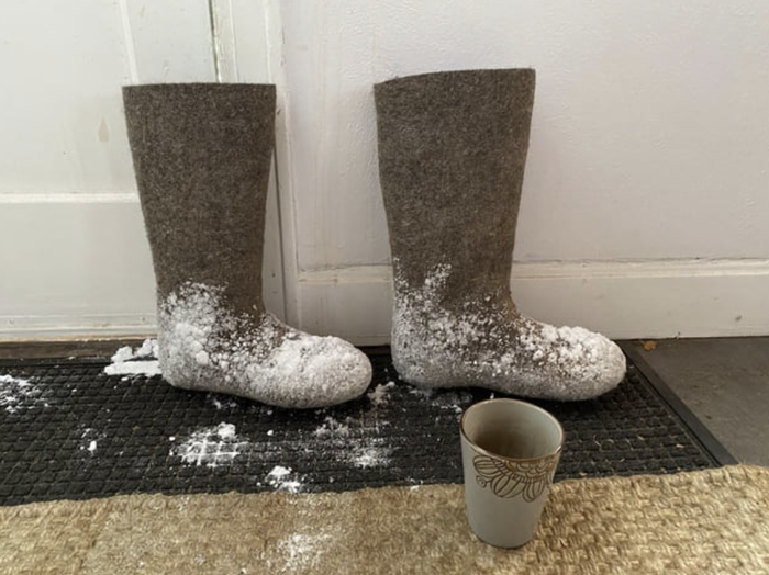 Calf-high boots with snow on them resting on a mat.