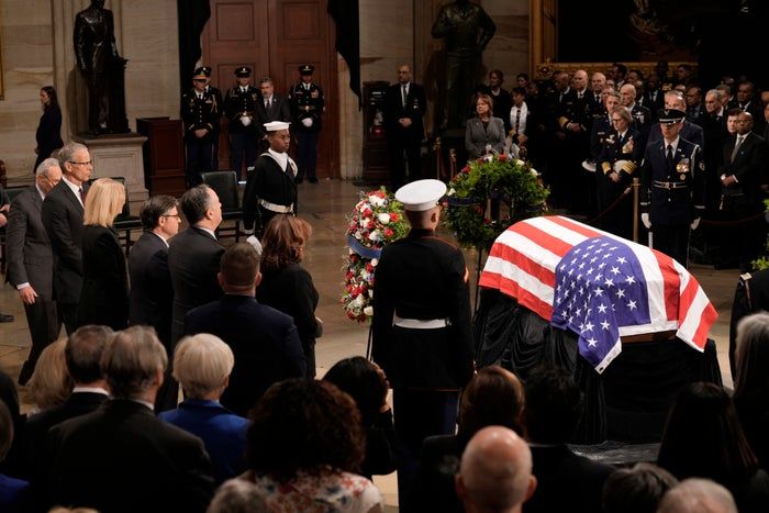 The funeral service for Jimmy Carter featured a solemn gathering, with military personnel standing guard beside a coffin draped in the American flag, all observed by a quiet audience indoors.