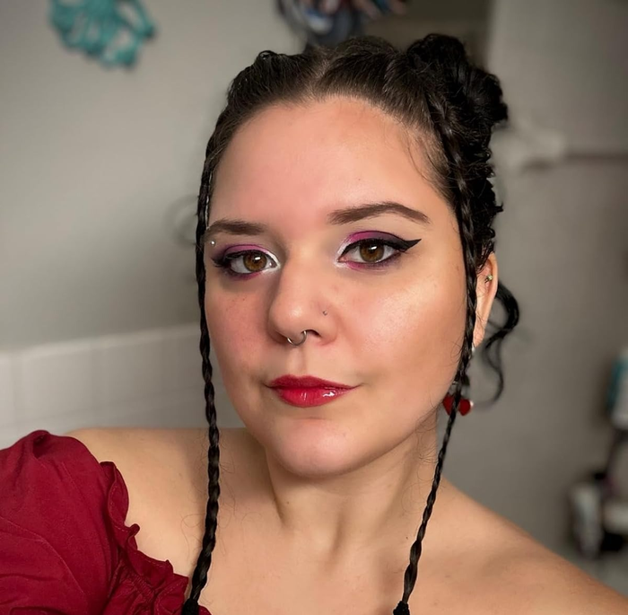 A reviewer with a full makeup look applies the clear NYX lip gloss over a red tint for a glossy finish