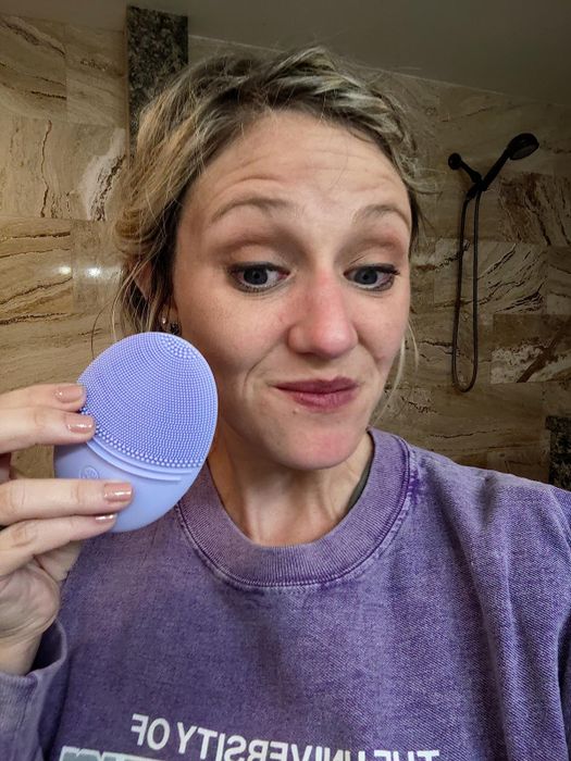 A reviewer holding a purple sonic facial cleanser