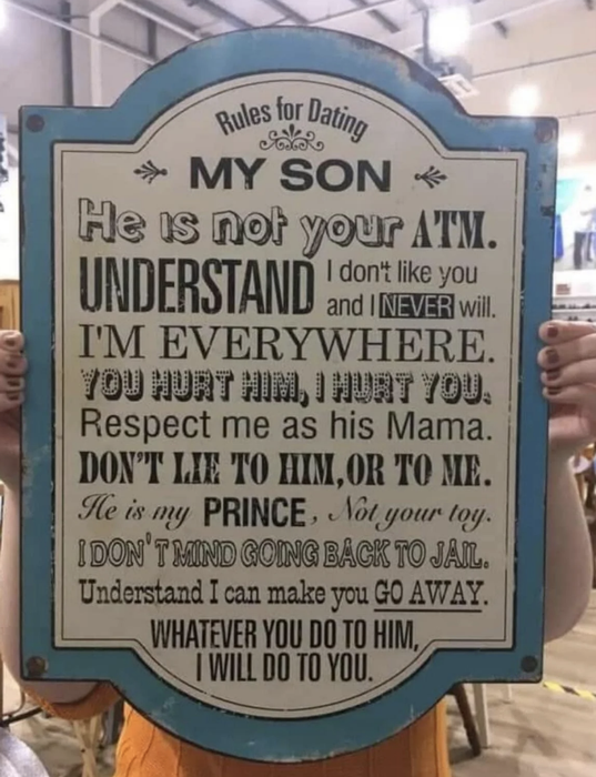 A person holding a sign titled 'Rules for Dating My Son' with lighthearted threats about protecting him.