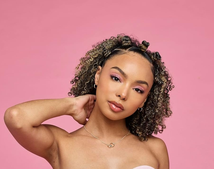 Model with curly hair striking a pose against a pink backdrop