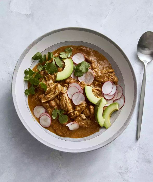 Slow Cooker Chicken Mole Chili, topped with radishes and avocado slices, served in a white bowl with a metal spoon placed on the side for easy eating.