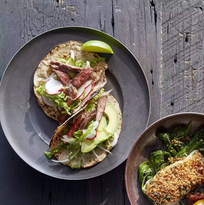 Two delicious garlic skirt steak tacos, topped with radishes and creamy avocado slices, served on a round gray plate.
