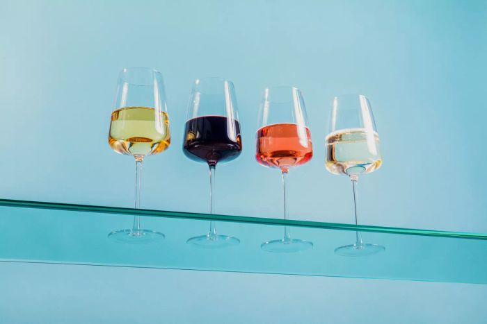 Four glasses of wine arranged neatly on a glass shelf set against a soft blue wall