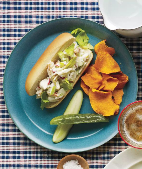 A single crab roll served with dill pickles and sweet potato chips on a blue plate