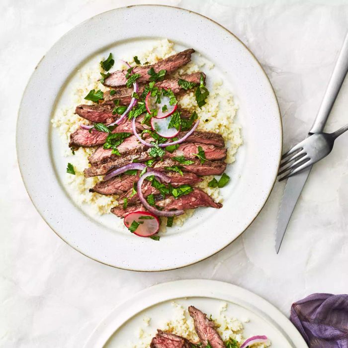 Five-Spice Steak with Couscous and Radishes, served on two white plates with metal utensils placed alongside.