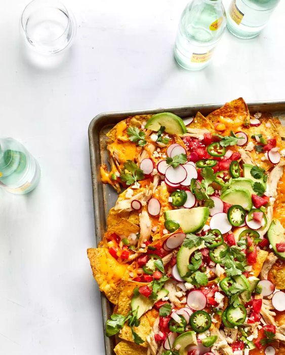 Cheesy Chicken Nachos topped with avocado and radish, served on a baking sheet.