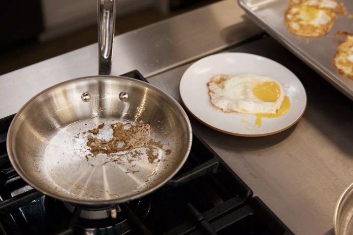 A fried egg served on a plate next to a pan from the All-Clad D5 Stainless Brushed 5-Ply Bonded Cookware Set.