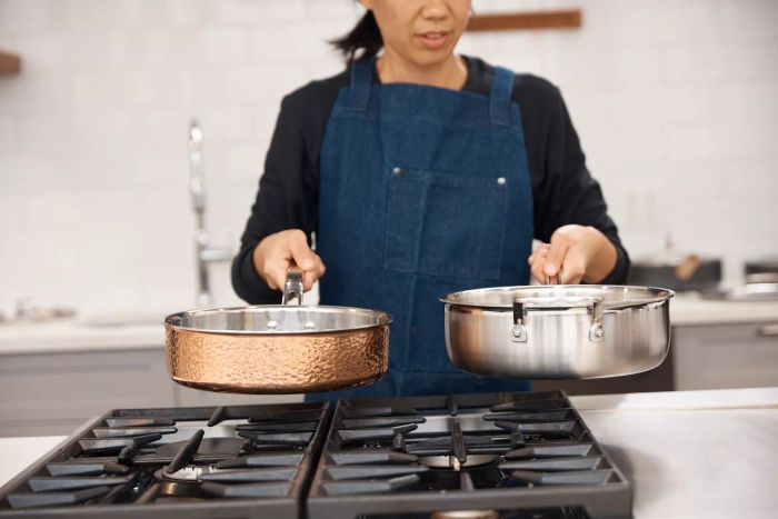 A person holding both a Cuisinart MultiClad Pro 12-Piece Triple-Ply Stainless Cookware Set sauté pan and a pan from a different brand.