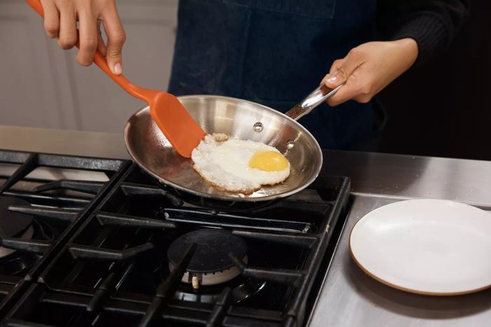 A person uses a spatula to lift a fried egg out of a pan from the All-Clad D5 Stainless Brushed 5-Ply Bonded 10-Piece Cookware Set.