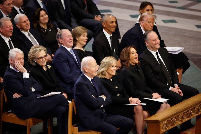 A group of well-dressed individuals seated at an event, smiling and actively engaged in conversation.
