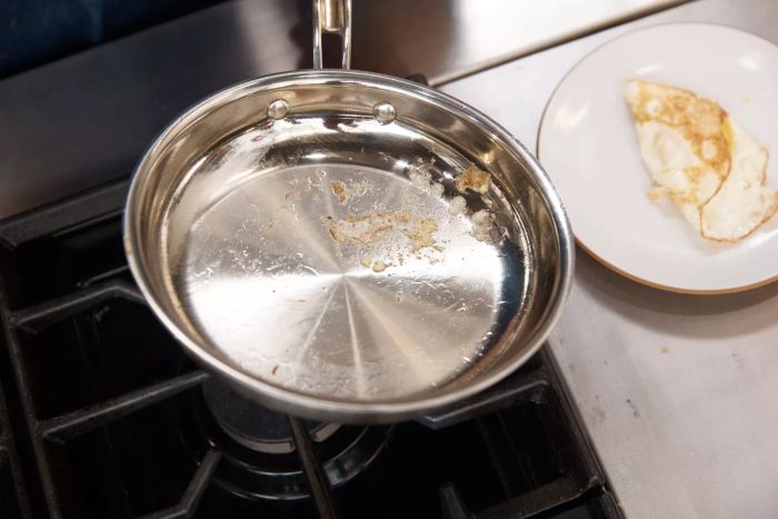 A Cuisinart MultiClad Pro 12-Piece Triple-Ply Stainless Cookware Set frying pan placed on the stovetop next to an egg on a plate.