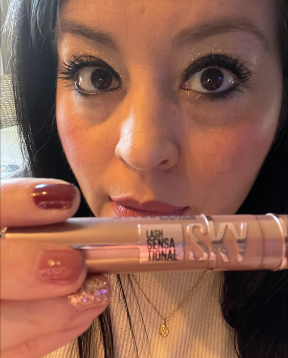A reviewer wearing black mascara while holding up the tube