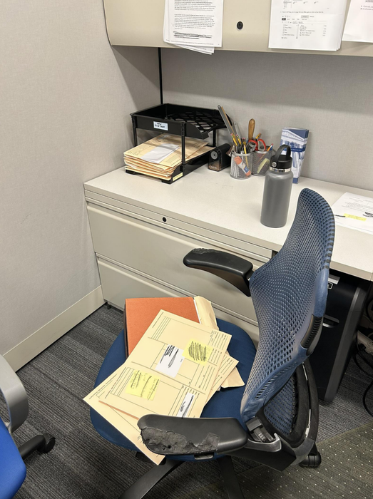 Stacks of paperwork piled on an office chair beside an organized desk.
