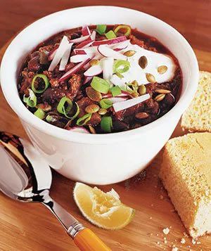 A bowl of beer chili topped with fresh scallions, accompanied by a side of cornbread.