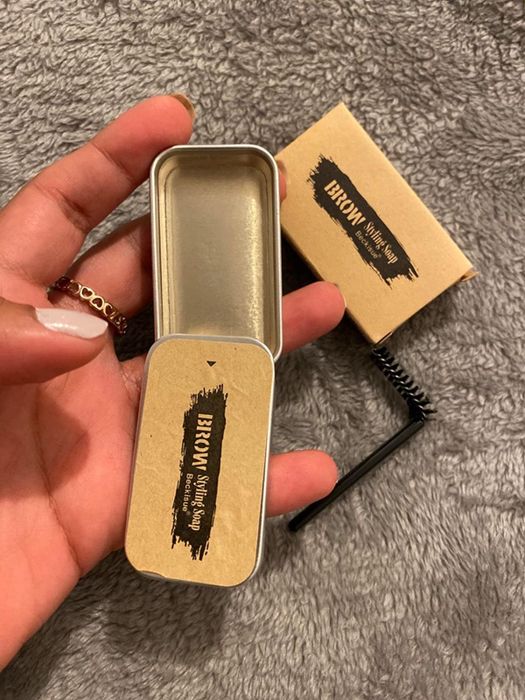 A reviewer is holding the kit in their hand, displaying that it includes both the soap and a brush for easy application.