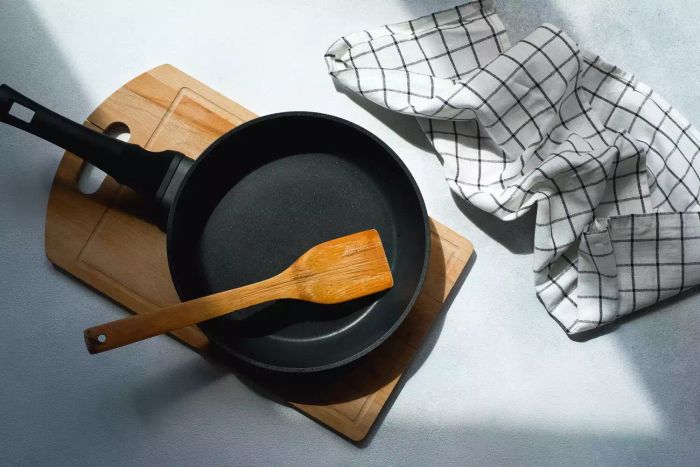A close-up shot of a cast-iron frying pan paired with a dish towel, set against a gray backdrop