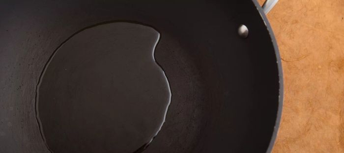 A cast-iron skillet with oil, displayed on a tan background