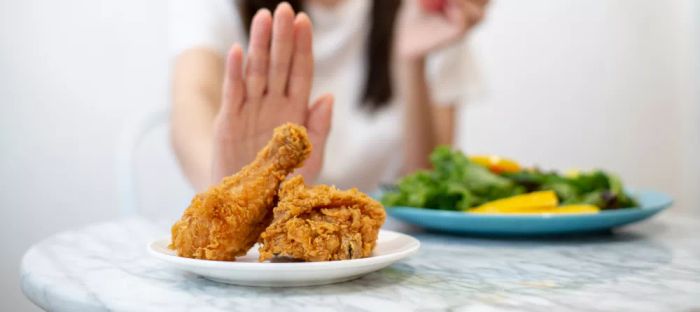 A woman turning down junk food like fried chicken or desserts, opting instead for healthier choices such as fresh fruits or vegetables, reflects the concept of dieting and maintaining good health.