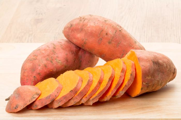 Two whole sweet potatoes and a sliced sweet potato placed on a table