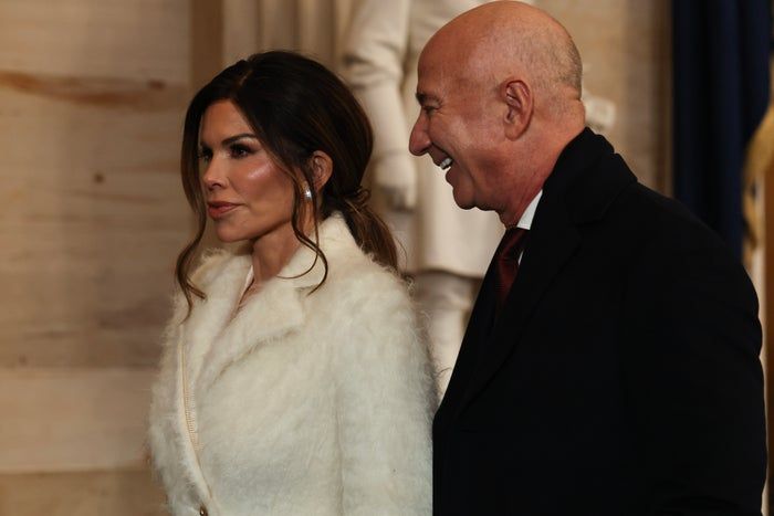 The couple, Lauren Sánchez and Jeff Bezos, are seen walking together in formal attire, with Lauren sporting a luxurious fur-like coat.