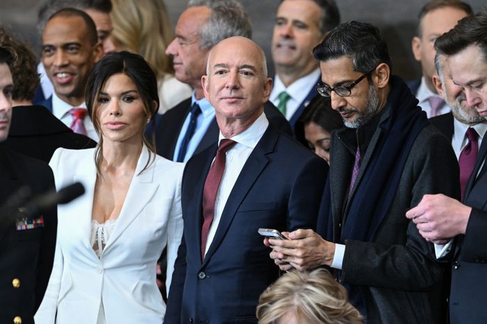 A group of impeccably dressed professionals gathers at a formal event, with one individual engrossed in their phone, capturing a moment from the business occasion.