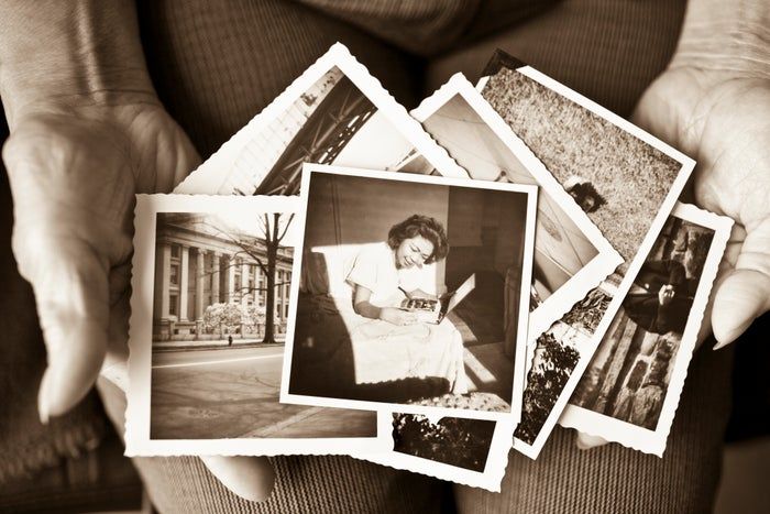 A person is holding a set of black-and-white photographs, showing various scenes with a woman smiling as she looks at a book.
