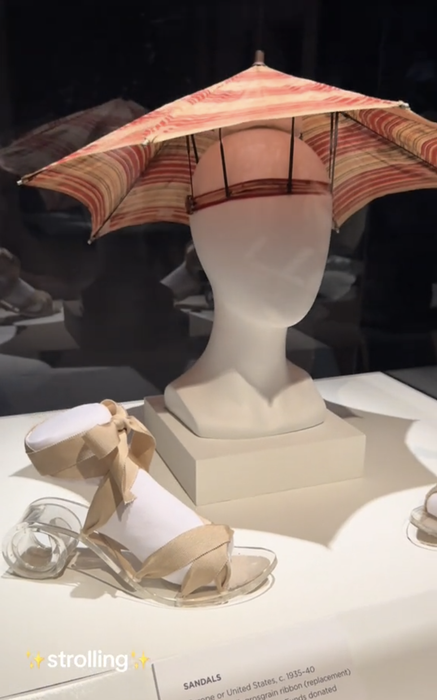 A display featuring an umbrella hat perched on a mannequin head, with ribbon-tied sandals positioned nearby. The text overlay reads: 