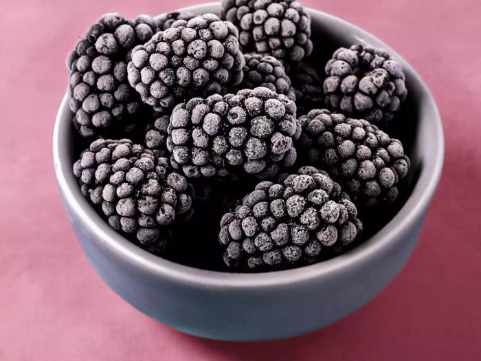 Frozen blackberries nestled in a bowl on a soft pink background