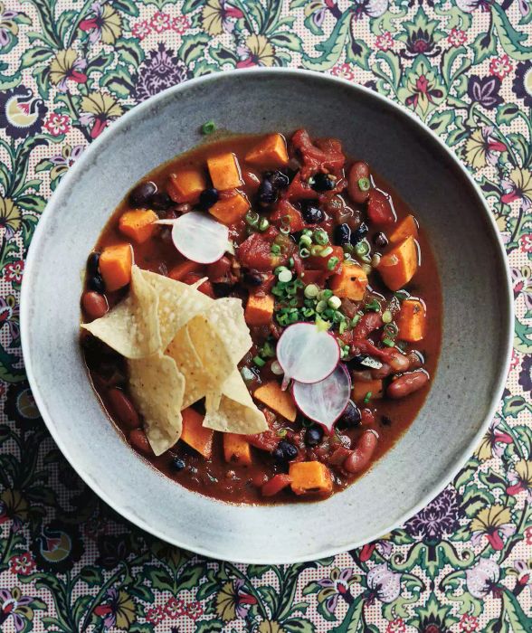 A bowl of slow-cooked vegetarian chili with sweet potatoes, beans, and tomatoes, topped with crunchy corn chips