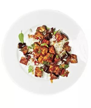 Eggplant and tofu stir-fried and garnished with fresh scallions, served on a white plate