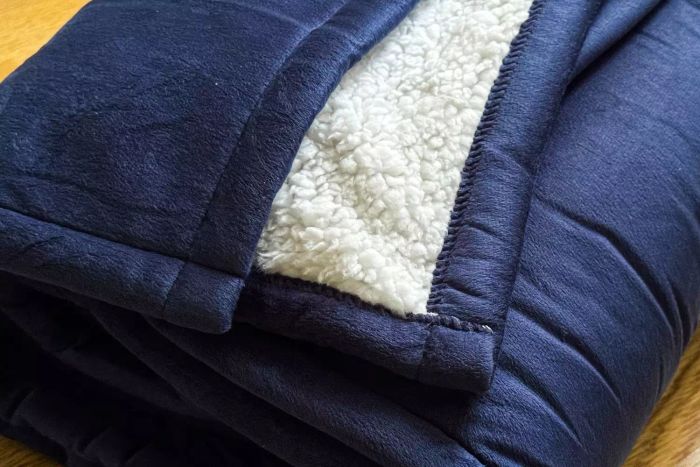 A detailed view of the Sunbeam Royal Mink Sherpa Heated Blanket folded neatly on the floor