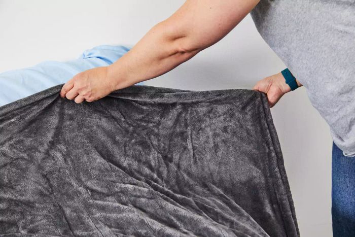 A person placing the Westinghouse Electric Throw Blanket onto a bed