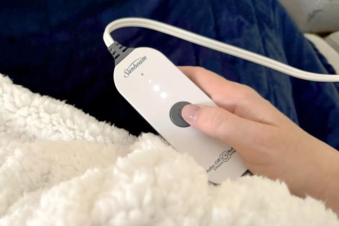 A person pressing the power button on the Sunbeam Royal Mink Sherpa Heated Blanket