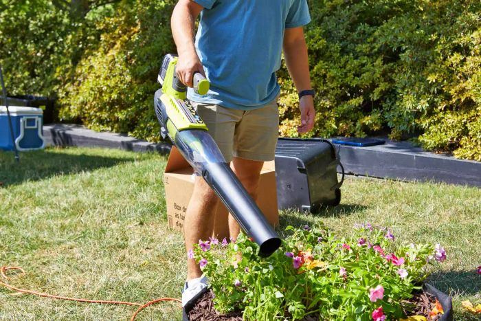 A person using the Ryobi ONE+ 18V 100 MPH 280 CFM Cordless Battery Variable-Speed Jet Fan Leaf Blower on a planter.