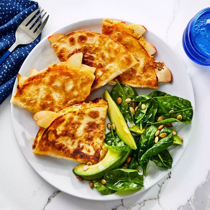 Top view of Apple Cheddar Quesadillas, sliced into triangles, accompanied by a fresh spinach-avocado salad on the side.