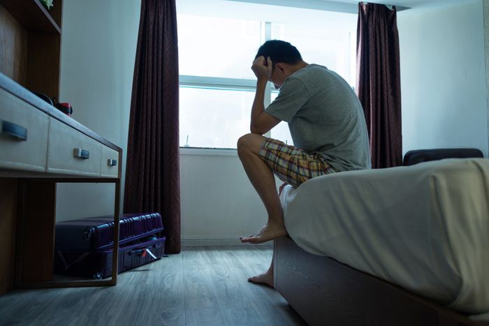 A man sitting on the edge of a bed, visibly distressed.