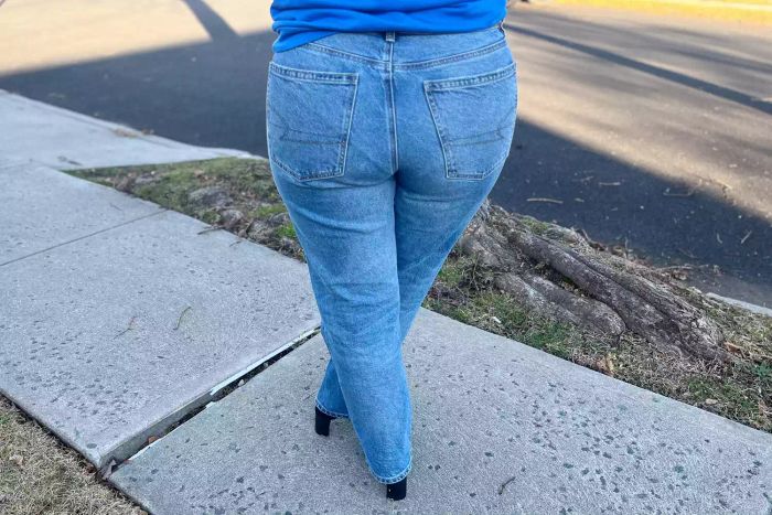 Image displays the back view of someone wearing American Eagle AE Stretch Super High-Waisted Ankle Straight Jeans outdoors