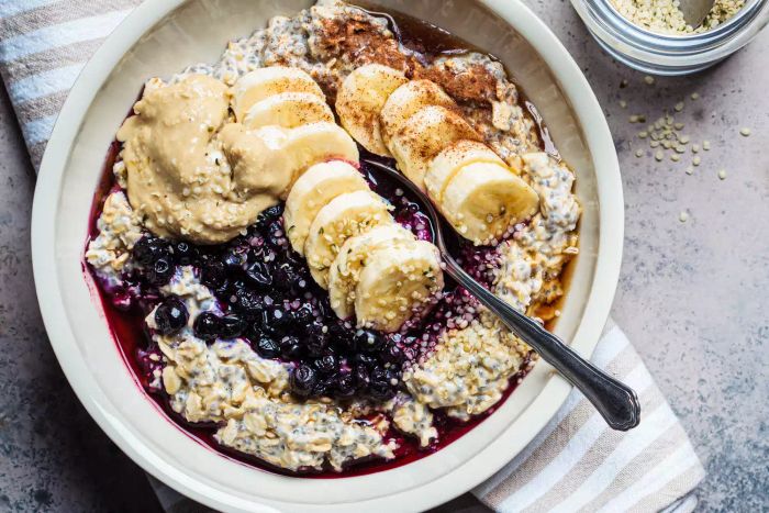 A cozy winter breakfast idea: overnight oats topped with banana, berries, chia seeds, sesame tahini, cinnamon, and syrup in a bowl.