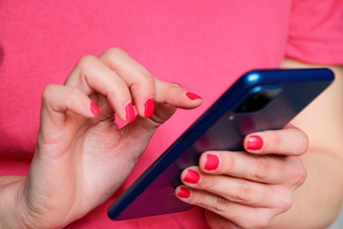 A person using a smartphone, with their hands in focus, displaying painted nails as they engage in touch-screen activities.