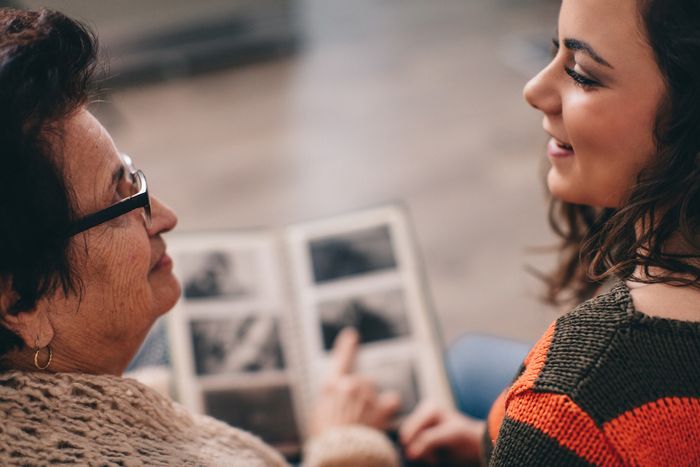 An elderly woman and a young lady flipping through a photo album together.